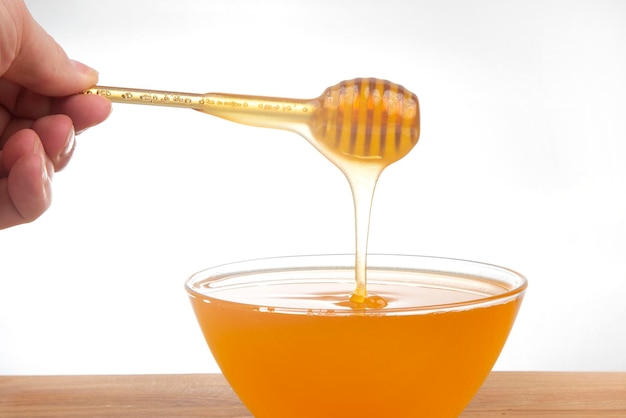 Miel fresca goteando de una cuchara en un plato transparente sobre un fondo blanco vitamina orgánica alimentos saludables