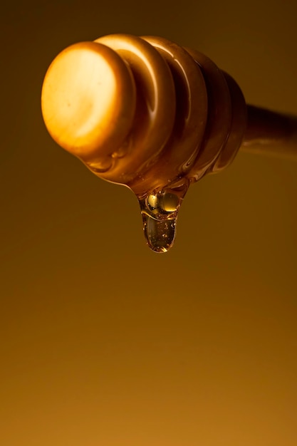 Foto la miel goteando de la percha de madera de la vara de miel macro disparado sobre un fondo amarillo oscuro