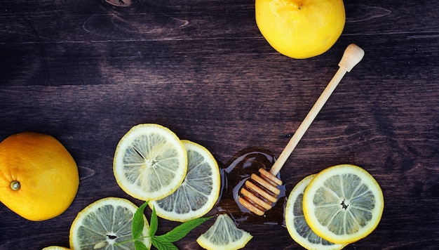 Foto miel y limón. palito de miel y rodajas de limón en rodajas sobre la mesa de madera. té en una taza y miel de lima dulce en un frasco.