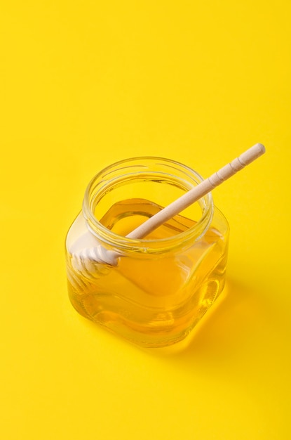 Miel líquida de la flor en el tarro de cristal con la cuchara de madera de la miel.