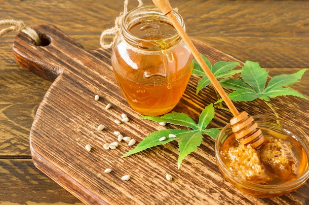 Miel orgánica fresca con hojas y semillas más profundas y de cannabis en la mesa de madera. Medicina alternativa de alimentación saludable.