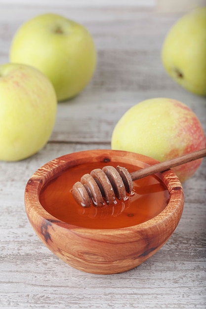 Miel en recipiente de madera con cucharón de miel y manzanas verdes sobre fondo blanco de madera vintage