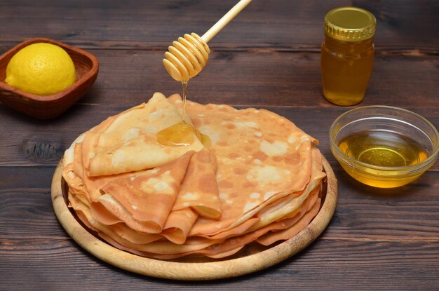 La miel se vierte de un cucharón sobre una pila de panqueques delgados para las vacaciones de Maslenitsa