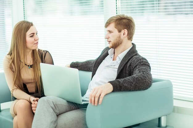 Miembros del equipo empresarial con una computadora portátil, discutiendo problemas laborales sentados en el sofá de la oficina en el vestíbulo de la oficina