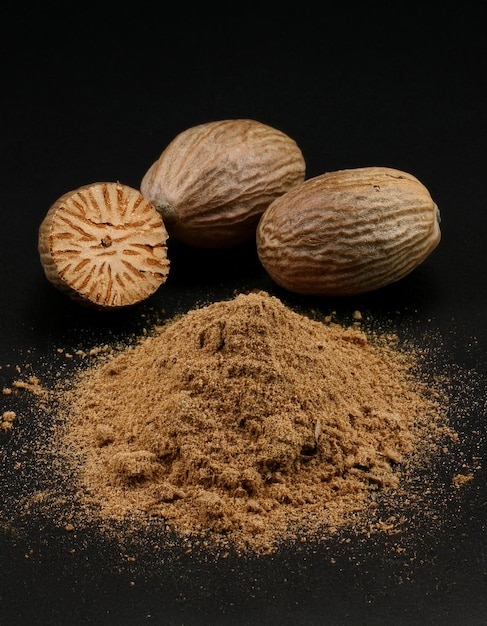 Migas de nuez moscada en polvo con algunos pedazos de nuez muscada aislados en fondo negro