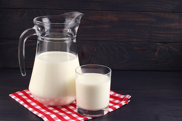 Milch in einem Krug und ein Glas auf dunklen Brettern