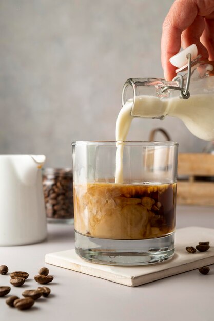 Milch in Glas mit Eiskaffee gießen Kaltes Erfrischungsgetränk im Sommer