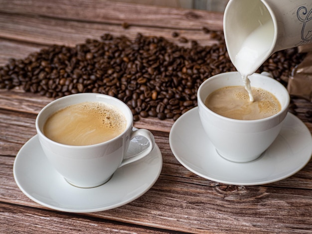 Milch in zwei weiße Tassen Kaffee gießen