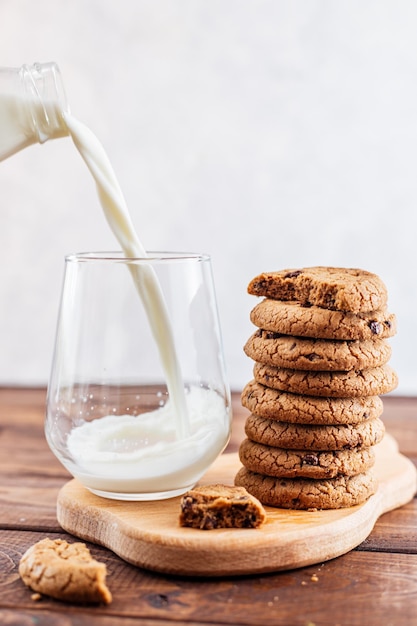 Milch wird aus einer Flasche auf dem Tisch neben einem Stapel Keksen in ein Glas gegossen. Frühstück mit Milch und Keksen