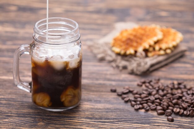 Milch wird in Kaffee gegossen. Kaffeebohnen auf dem Hintergrund