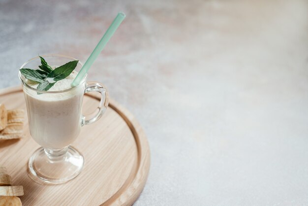 Milchbananenshake mit Minzblättern in einem Latte-Glas mit Griff auf hellem Hintergrund mit Kopierraum