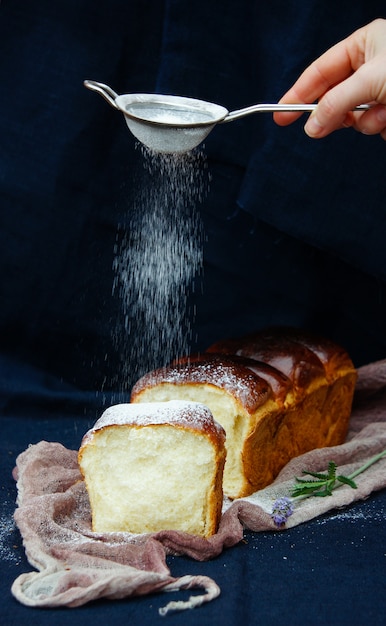 Milchbrotlaib, weibliche Hand mit Puderzucker bestreuen