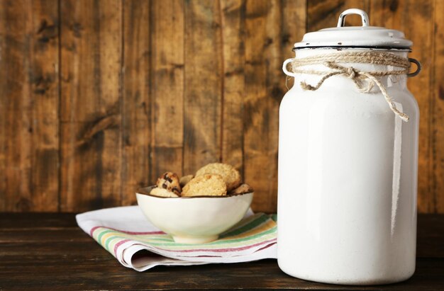 Milchdose mit einer Schüssel Kekse auf einem Geschirrtuch auf rustikalem Holzhintergrund
