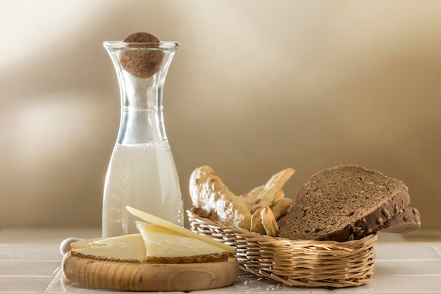 Milchflasche und Weidenkorb mit verschiedenen Brötchen Roggenbrot und Pfeifenkrapfentisch mit Käse