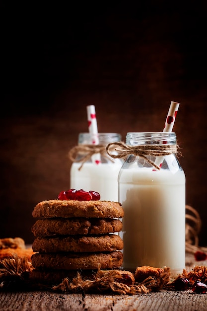 Milchgetränke in Glasflaschen, knusprige Kekse mit Granatapfelkernen, Vintage-Holzhintergrund, rustikaler Stil, selektiver Fokus