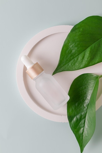 Milchglas-Kosmetikflasche mit Tropfer auf grauem Hintergrund mit tropischen Blättern Naturkosmetik-Konzept natürliche ätherische Öle und Hautpflegeprodukte