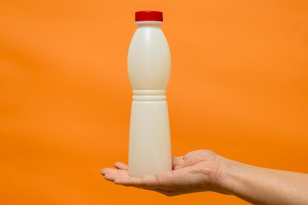 Milchjoghurtflasche in der Hand des Mannes mit orangefarbenem Hintergrund