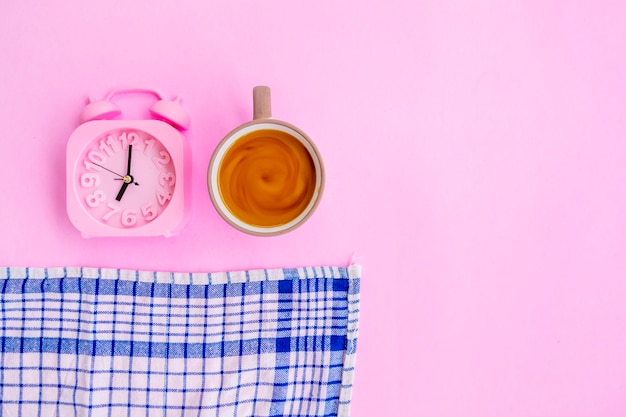 Milchkaffee, blaues Tuch und Wecker einzeln auf rosafarbenem Hintergrund, minimale Konzeptidee.
