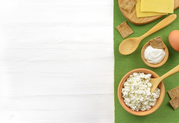 Milchprodukte in Holzschale für gesundes Frühstück auf weißem Holztisch. Sauerrahm, Hüttenkäse, Ei, Käse. Draufsicht mit Kopienraum