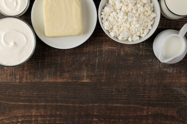 Milchprodukte. Milch, Sauerrahm, Käse, Butter und Hüttenkäse auf einem braunen Holztisch. Ansicht von oben. Rahmen. Platz für Text