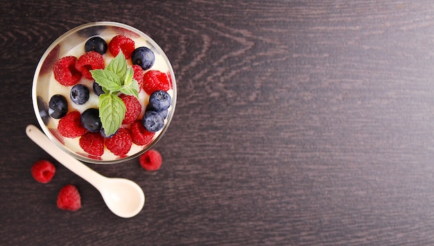 Milchpudding mit Beeren in einem Glas auf einem schwarzen Hintergrund