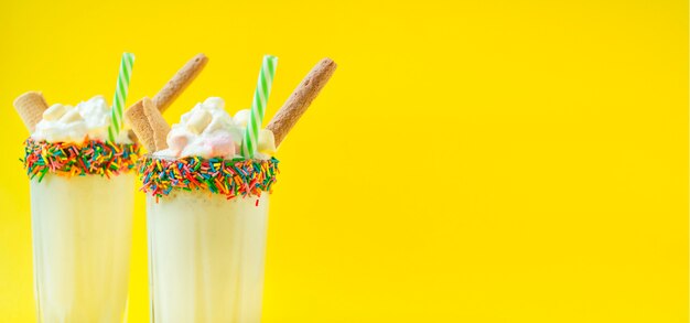 Milchshake mit Eis und Schlagsahne, Marshmallows, Waffeln, serviert in einer Glasschale mit Gebäckdressing. Sommercocktail. Hellgelber Hintergrund. Banner. Speicherplatz kopieren.