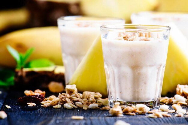 Milchsmoothies mit selektivem Fokus des dunklen Hintergrundes der Banane, Ananas und Granola