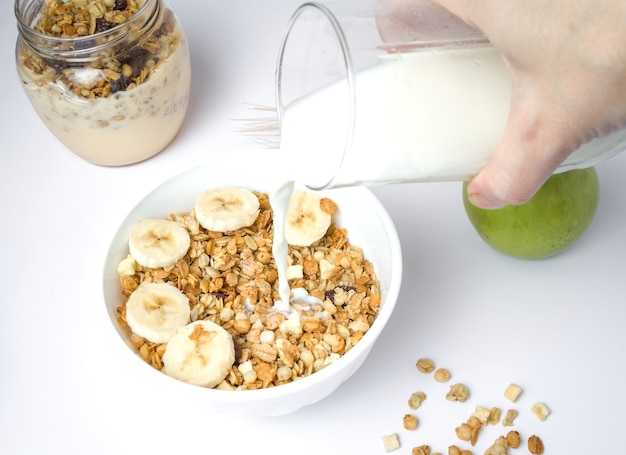 Milchspritzen in einer Schüssel mit frischem Müsli mit einer Mischung aus Weizen, Hafer und Kleie mit getrockneten Früchten und Nüssen auf weißem Grund.