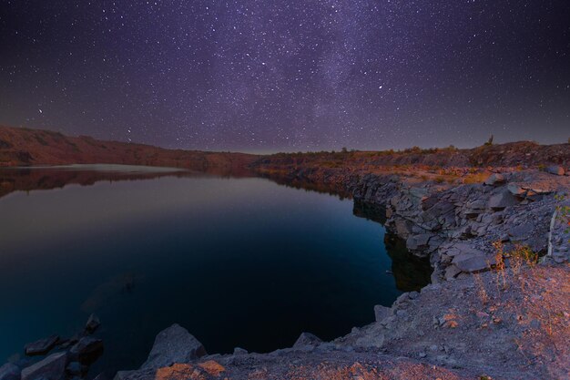 Milchstraße über einem See in einem Granitsteinbruch in der Nacht Sommerlandschaft mit riesigen Felsbrocken Bäume lila Himmel mit Milchstraße und Sternen schöne Spiegelung im Wasser Ukraine Raum und Natur