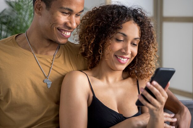 Milenaria pareja afroamericana en el sofá mirando la pantalla del teléfono inteligente