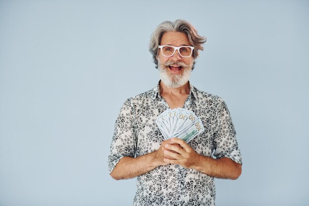 Foto milionário com dinheiro nas mãos homem moderno elegante sênior com cabelos grisalhos e barba dentro de casa