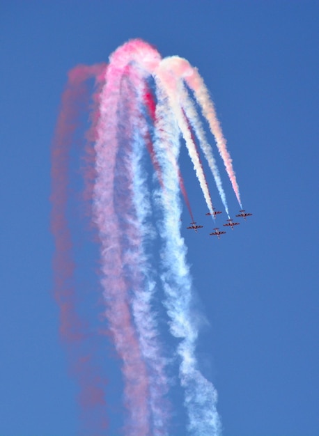 Militärische Kampfflugzeuge fliegen in einer Gruppe mit Rauch am blauen Himmel