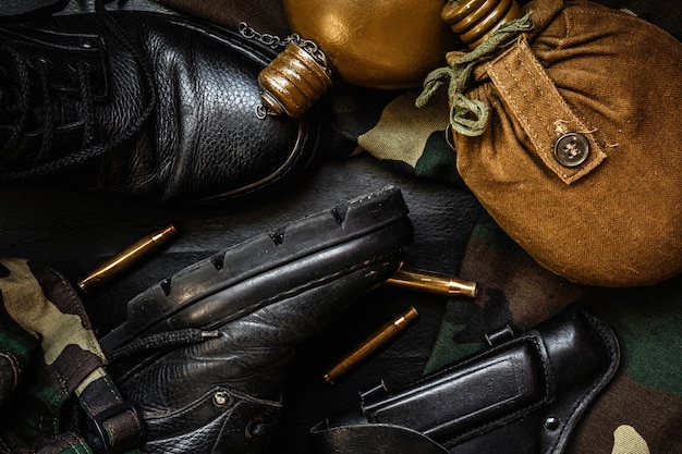 Militärische Tarnung Uniform und Stiefel. Ein Satz Militärartikelflaschengewehr auf einem dunklen Hintergrund