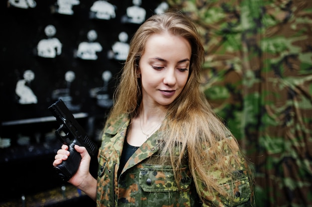 Militärmädchen in der Tarnungsuniform mit dem Gewehr zur Hand gegen Armeehintergrund auf Schießstand.