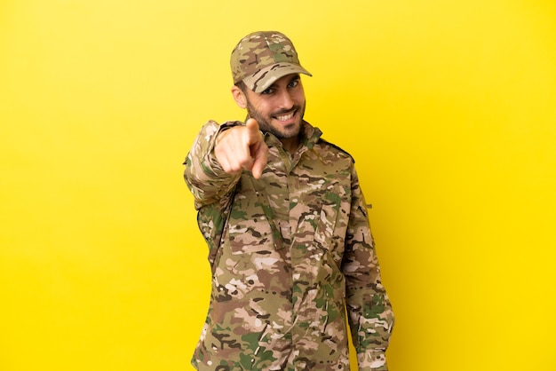 Militärmann, der auf gelbem Hintergrund isoliert ist, zeigt mit einem selbstbewussten Ausdruck mit dem Finger auf Sie