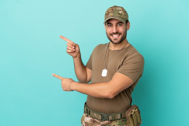 Militar com dog tag isolado em fundo azul apontando o dedo para o lado e apresentando um produto