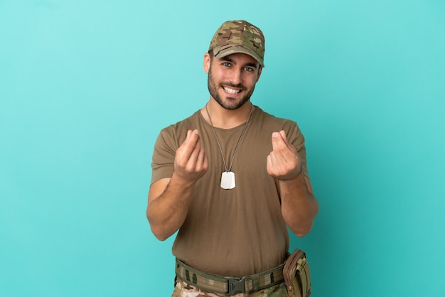 Militar com dog tag isolado em fundo azul fazendo gesto de dinheiro