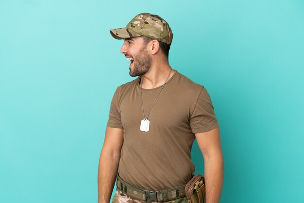 Militar com dog tag isolado em fundo azul rindo em posição lateral