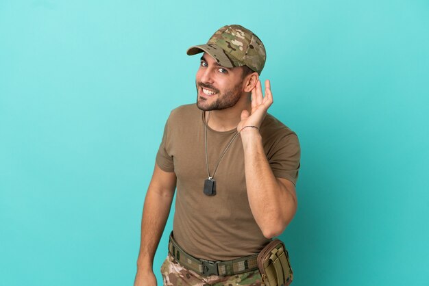 Militar com etiqueta de cachorro isolada em fundo azul, ouvindo algo colocando a mão na orelha