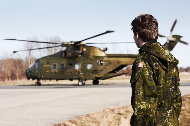 Militar del ejército o soldado con un helicóptero al aire libre para el transporte Guerra de Dinamarca y misión piloto Hombre para vuelo de combate o servicio de la fuerza aérea con uniforme de camuflaje para vigilar o patrullar