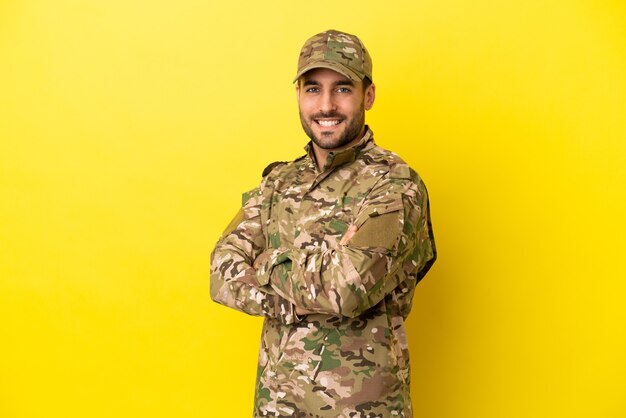 Militar isolado em fundo amarelo com os braços cruzados e olhando para a frente