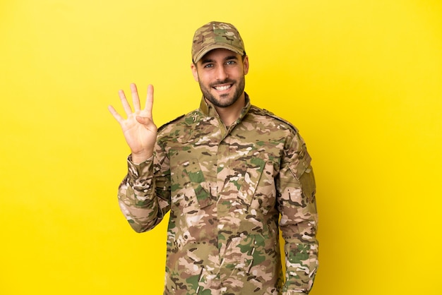 Militar isolado em um fundo amarelo feliz e contando quatro com os dedos