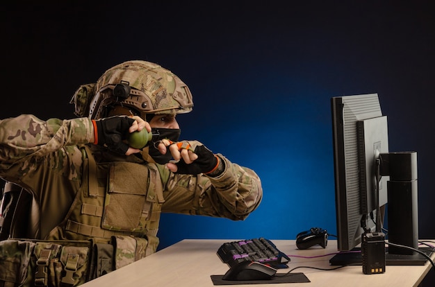 Los militares en uniforme sentados frente a una computadora son guerra cibernética, jugando, lanzando una granada