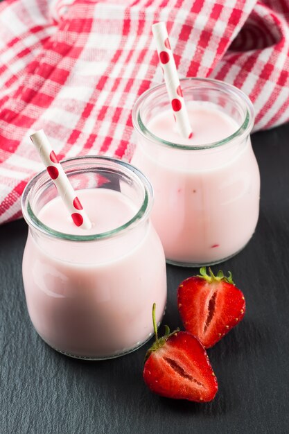 Foto milk-shake de morango na jarra de vidro com canudo na superfície de ardósia preta.