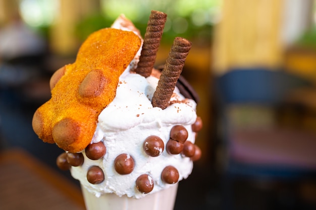 Milk-shake fresco com biscoitos e bolas de chocolate. Milk-shake em um copo de vidro sobre uma mesa em uma plataforma de rua em um café. Bebidas refrescantes de verão.