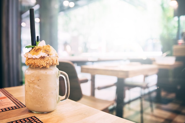 Milkshake de banana no topo com crumble de maçã e fatias de banana na mesa de madeira