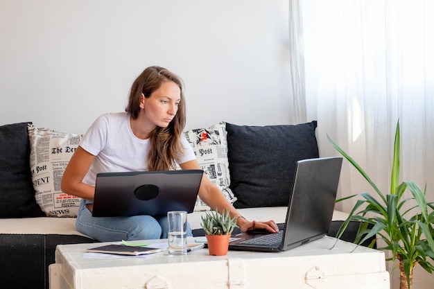 Millennial Frau arbeitet zu Hause, Sitze in der Nähe von Laptop-Computer mit Notebook, Glas Wasser auf weißem Tisch im Heimarbeitsbereich.