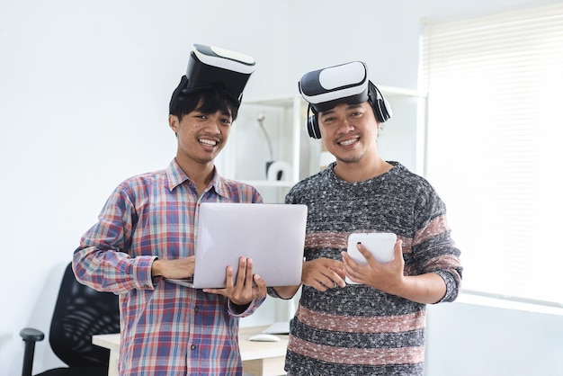 millennials em óculos de realidade virtual segurando laptop e tablet enquanto olham para a câmera sorrindo