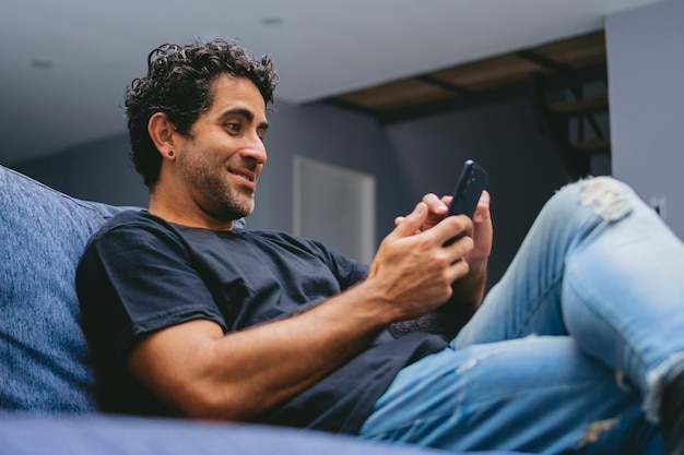 Millonario latino de mediana edad sentado en su sala de estar viendo sus redes sociales desde su teléfono celular Copiar espacio