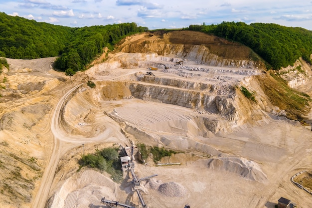 Mineração a céu aberto de materiais de pedra e areia de construção com escavadeiras e caminhões basculantes.